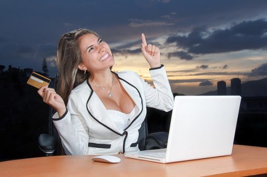business woman with credit card and laptop, smiling and pointing up